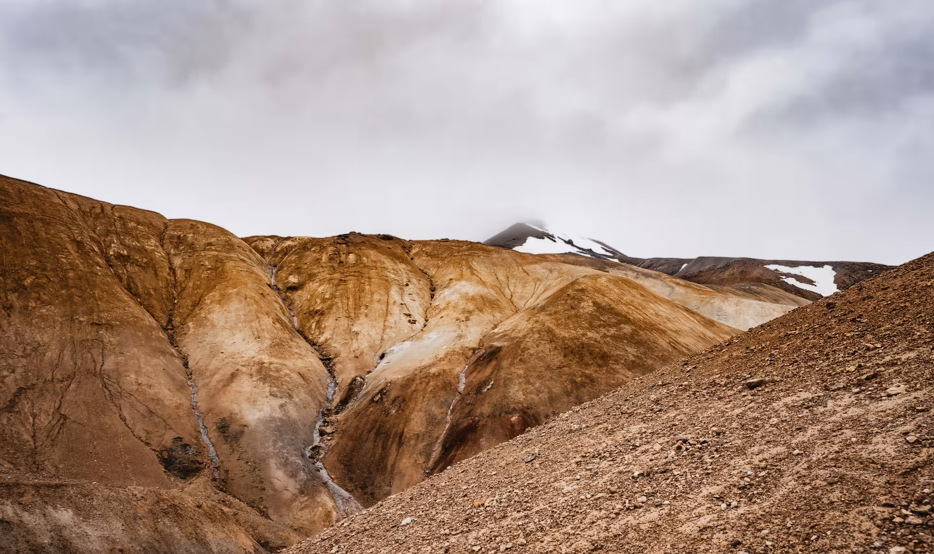 Rugged ochre and brown geothermal highland mountains with snow patches under overcast skies at Kerlingarfjoll, Iceland
