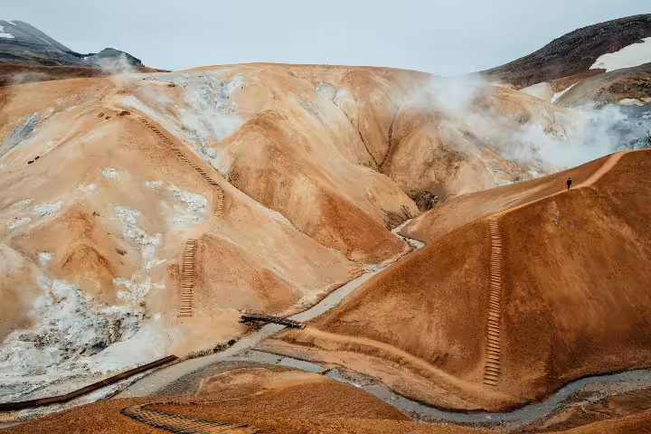 Steaming orange geothermal highlands of Kerlingarfjoll with wooden pathways and lone hiker on ridge
