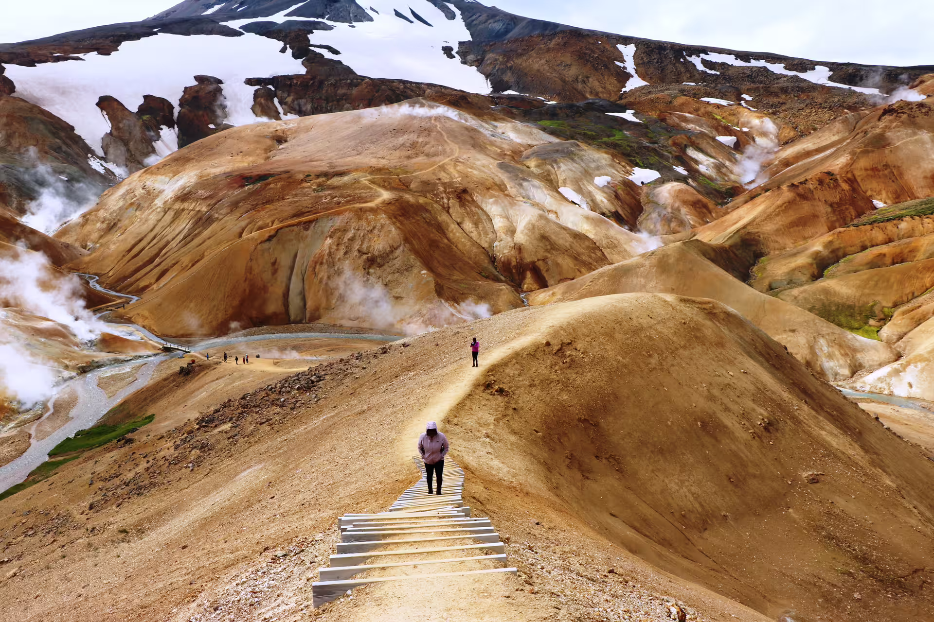 Hiker on wooden boardwalk trail through colorful geothermal rhyolite mountains at Kerlingarfjoll Highland
