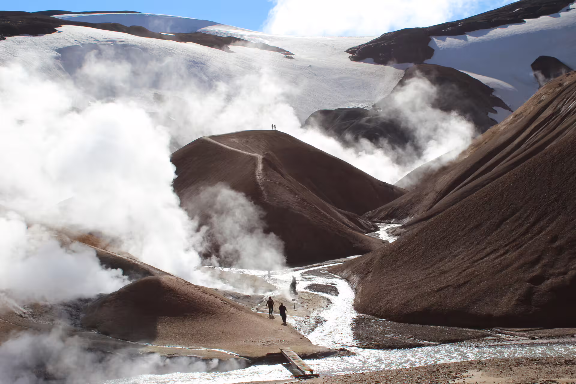 Hikers walking through steaming geothermal vents at Kerlingarfjoll highlands with snow-capped mountains