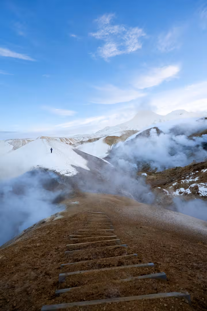 Steaming geothermal vents along a wooden-stepped trail in Kerlingarfjoll highlands with snow-covered mountains