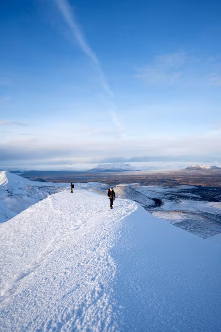 Two hikers walking along a snowy mountain ridge in Kerlingarfjoll Highlands under a clear blue sky