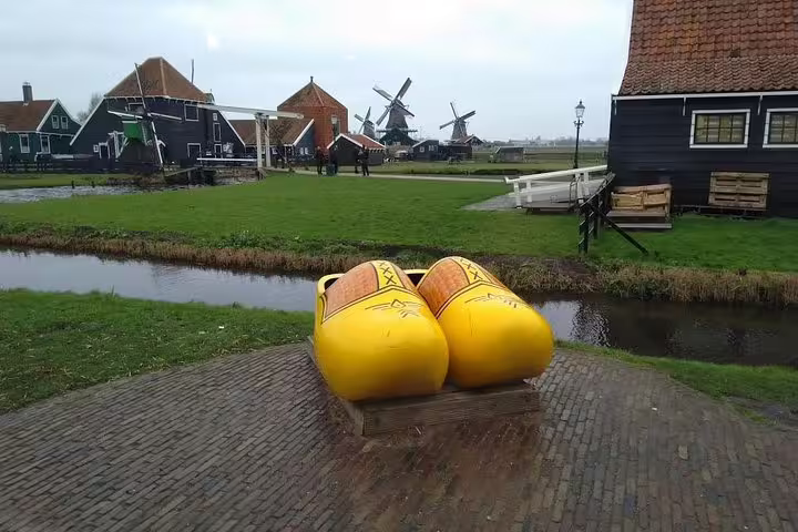 Giant yellow clogs by canal with Zaanse Schans windmills, stop on Keukenhof tulip tour from Amsterdam