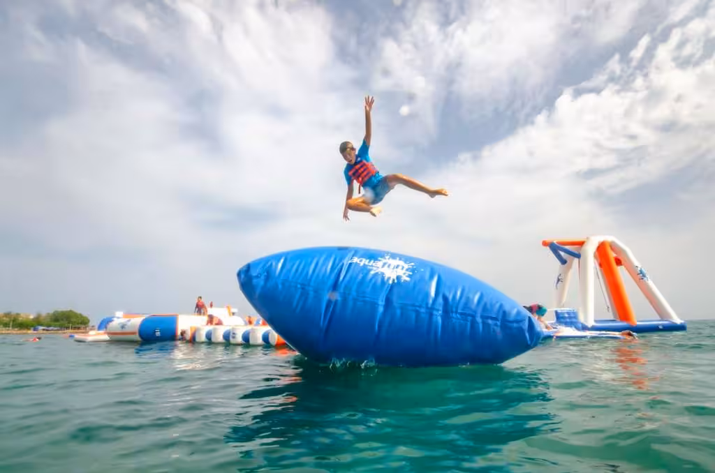 Kid in life vest leaping off a giant inflatable blob at an outdoor inflatable waterpark on the ocean