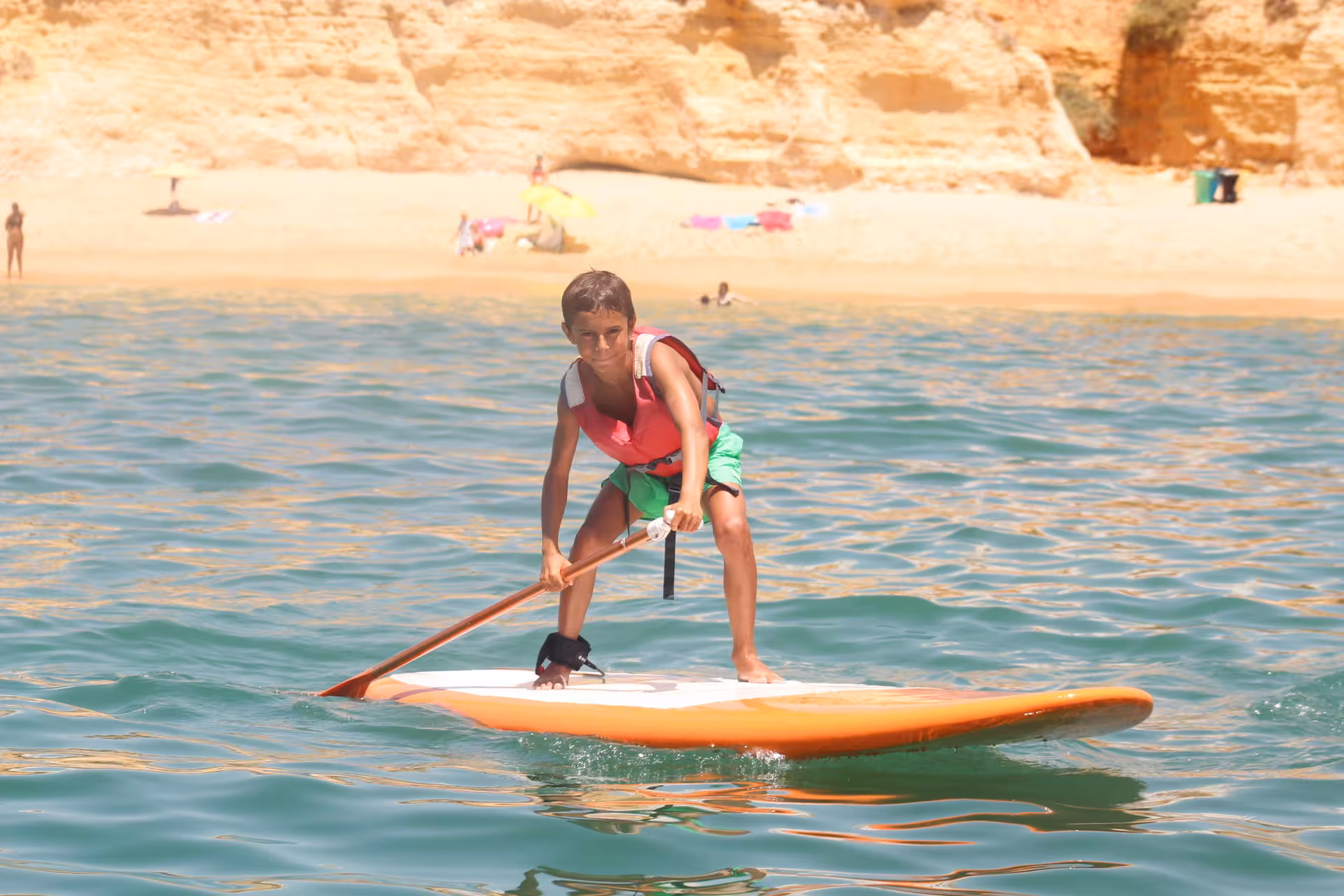 Young kid in a life vest paddling a stand up paddle board rental near a scenic rocky beach cliff