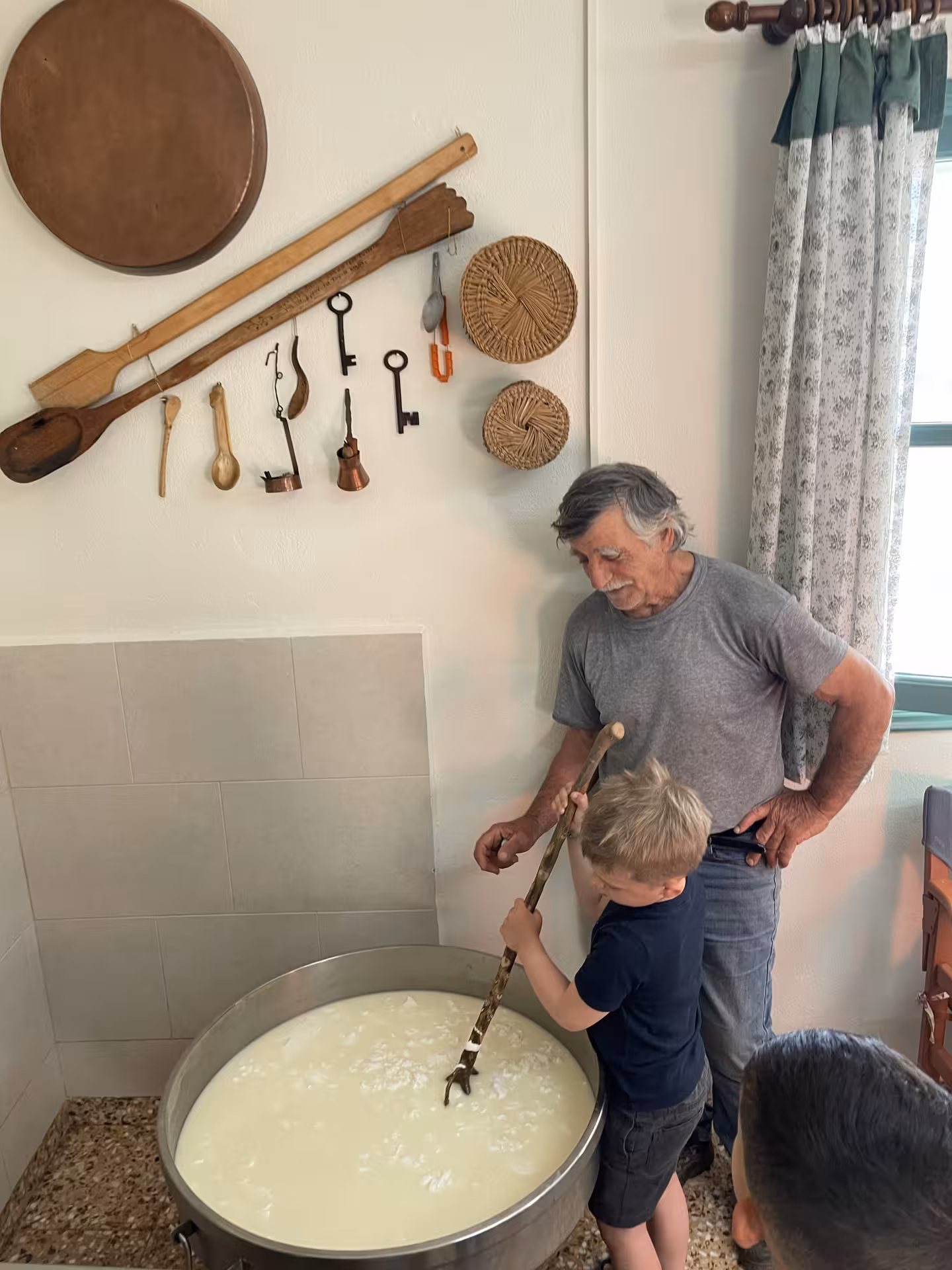 Child stirs fresh milk in a large vat with local guide on Kids First farm experience, learning traditional cheese making