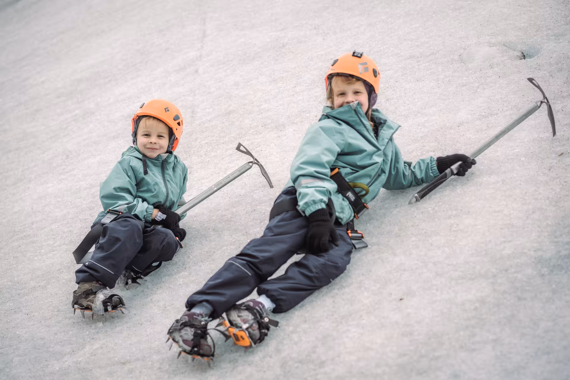 Two kids in helmets and crampons sitting on glacier ice during a family-friendly glacier hike in Iceland