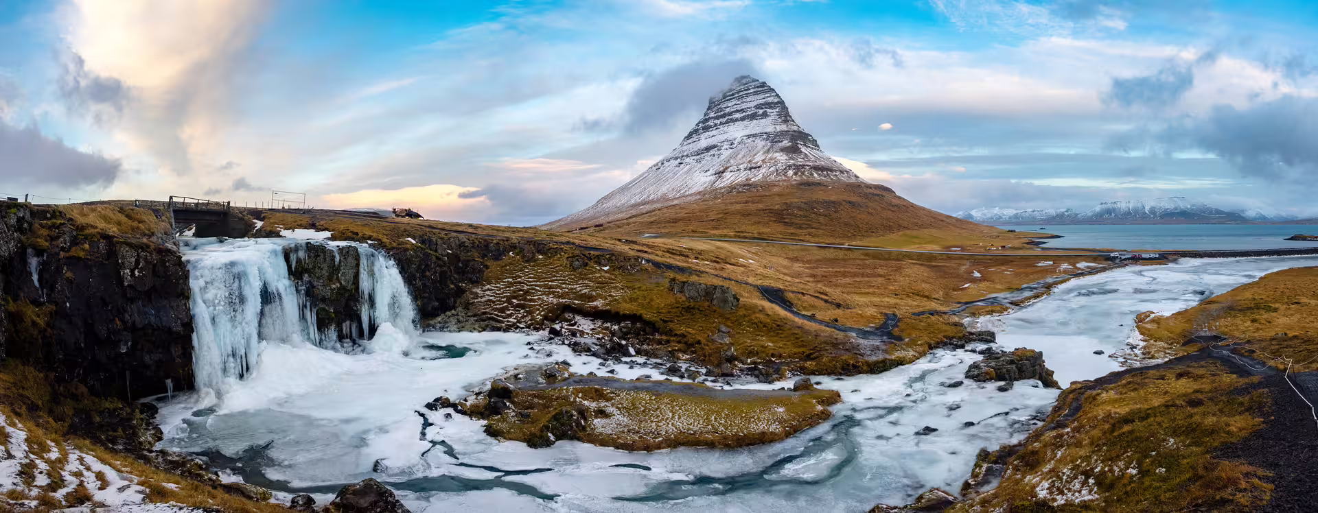 Kirkjufell mountain with partially frozen Kirkjufellfoss waterfall and icy river in Iceland winter landscape