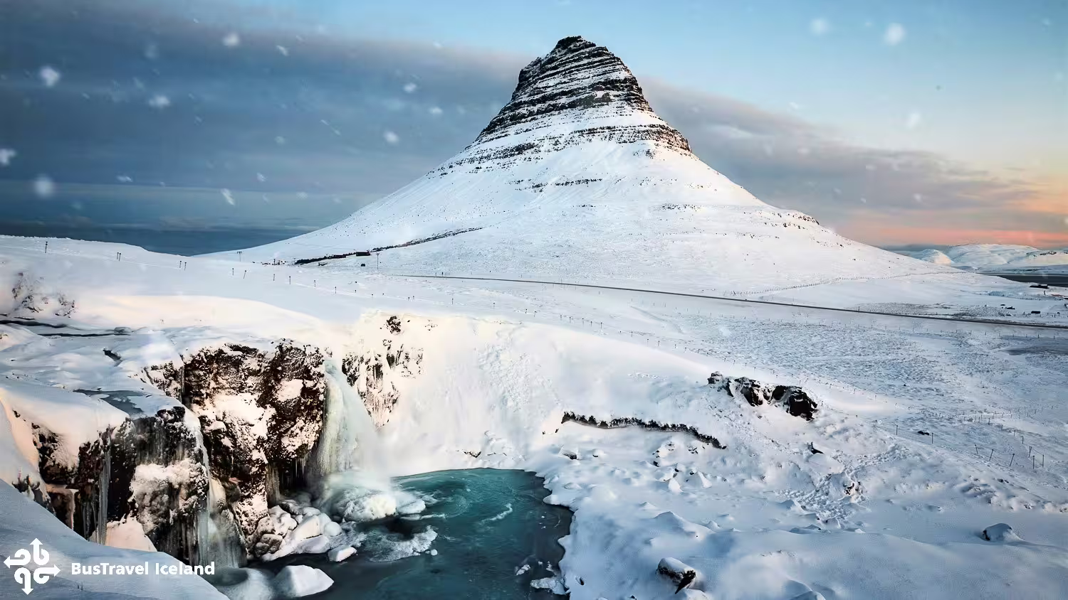 Kirkjufell mountain covered in snow with frozen waterfall and icy blue pool in Snaefellsnes Peninsula, Iceland