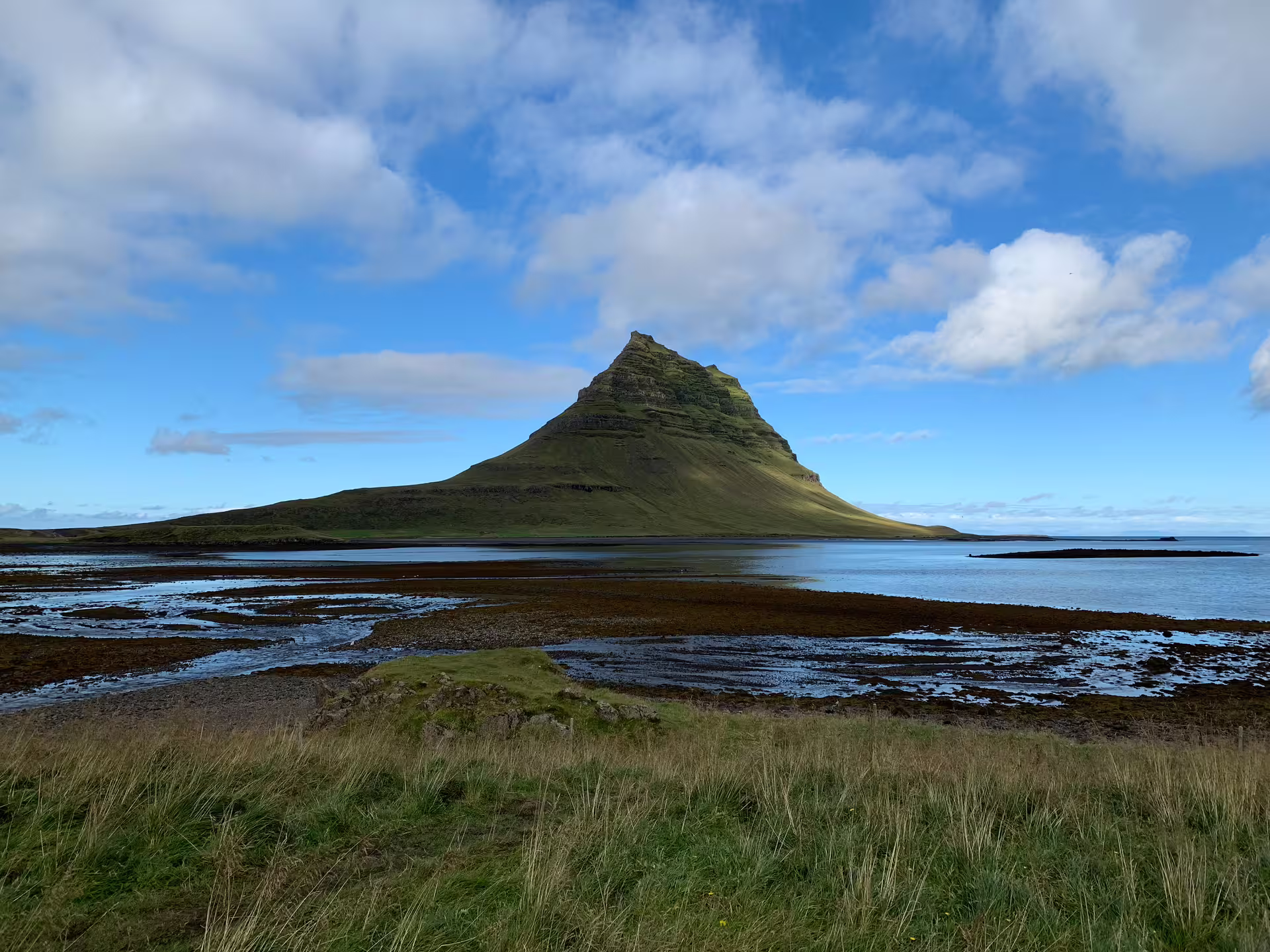 Kirkjufell mountain rising above coastal wetlands under blue sky in Iceland