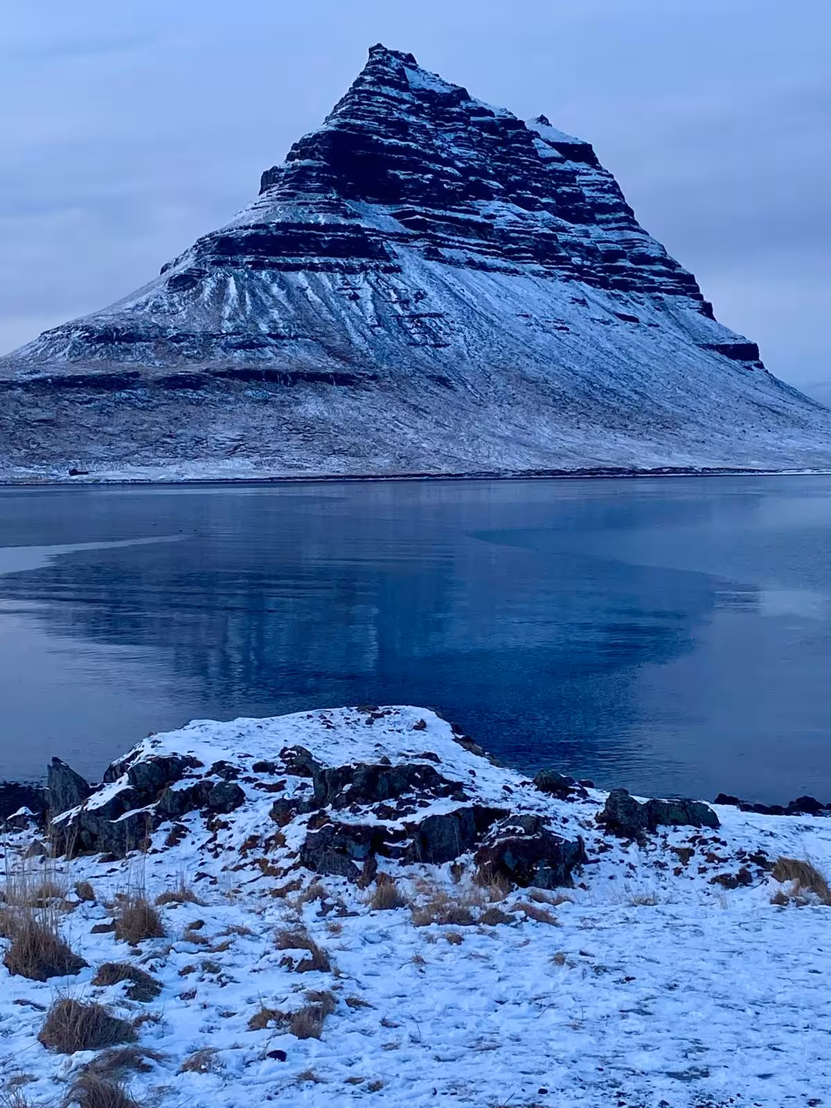 Snow-dusted Kirkjufell mountain reflected in calm fjord waters, Snæfellsnes Peninsula, Iceland in winter