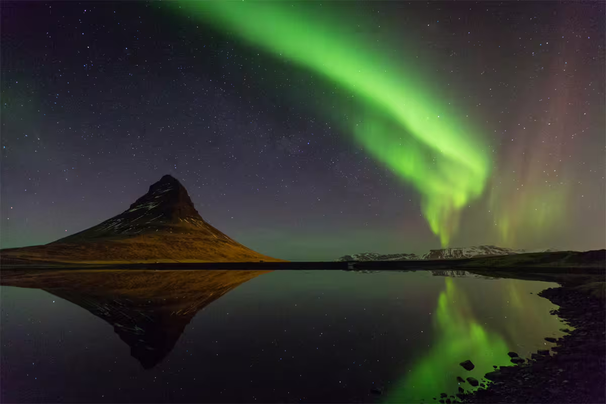 Aurora borealis dancing over Kirkjufell mountain reflected in calm water, Snaefellsnes Peninsula, Iceland