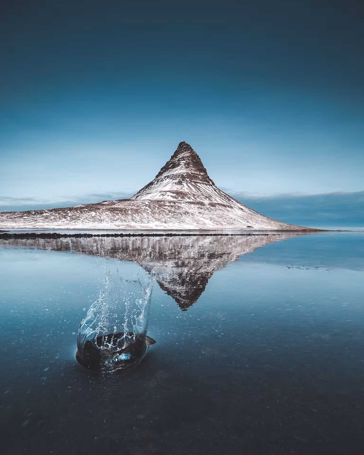 Kirkjufell mountain reflected in still water with a fish leaping in the foreground, Snaefellsnes Peninsula, Iceland