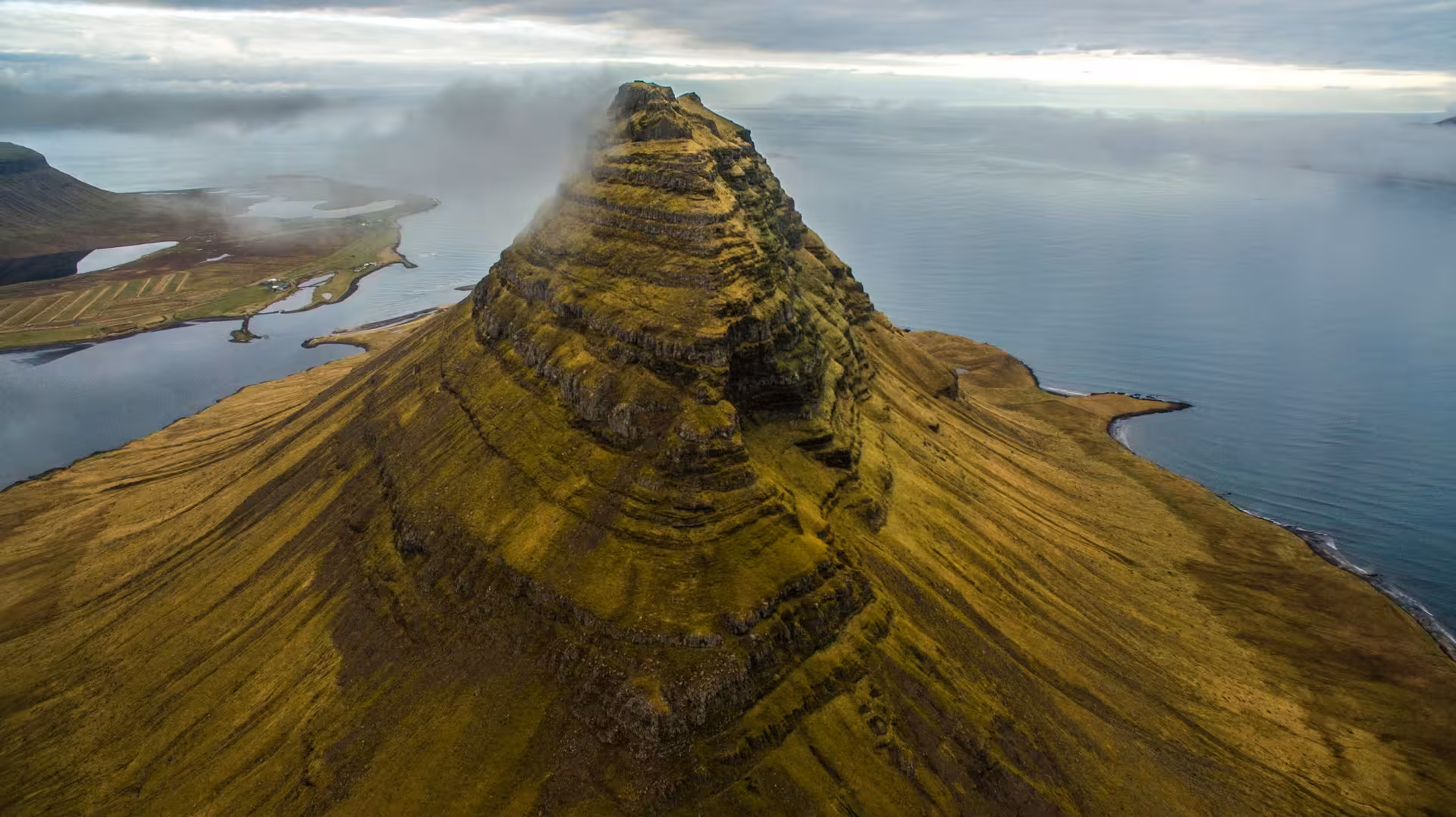 Aerial view of Kirkjufell mountain peak with moss-covered slopes and ocean coastline, Snaefellsnes Peninsula, Iceland