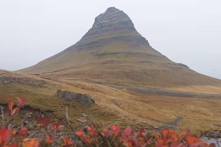 Kirkjufell mountain with distinctive peaked summit on Snaefellsnes Peninsula, Iceland, with red autumn foliage in foreground