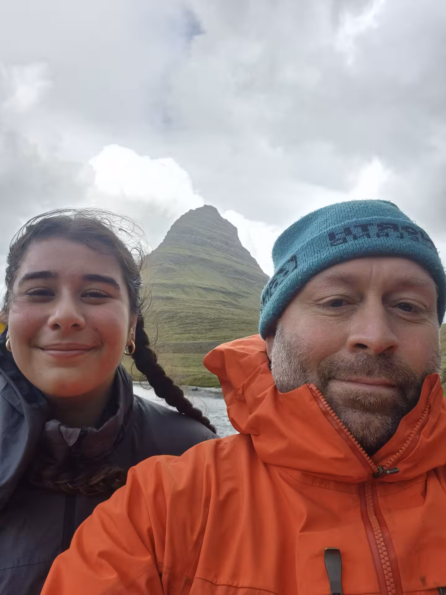 Two travelers smiling with Kirkjufell mountain behind them on Snaefellsnes Peninsula, Iceland