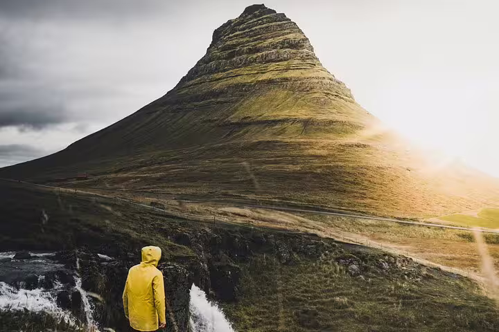 Person in yellow raincoat gazing at Kirkjufell mountain with waterfall in Snaefellsnes, Iceland