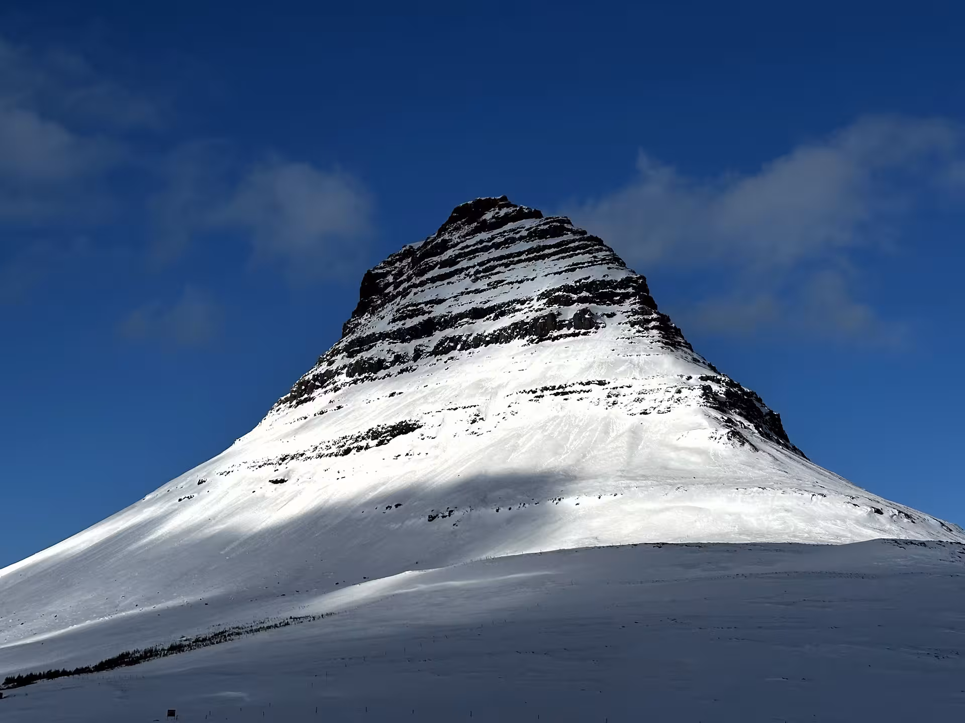 Snow-covered Kirkjufell mountain with layered rock peak against blue sky on Snaefellsnes Peninsula