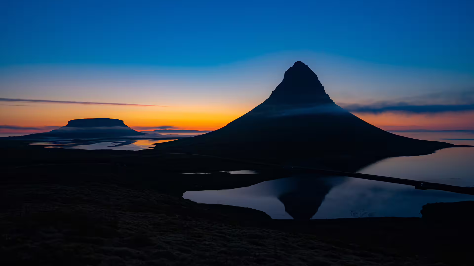 Kirkjufell mountain silhouette reflected in calm water at sunset, Snaefellsnes Peninsula, Iceland