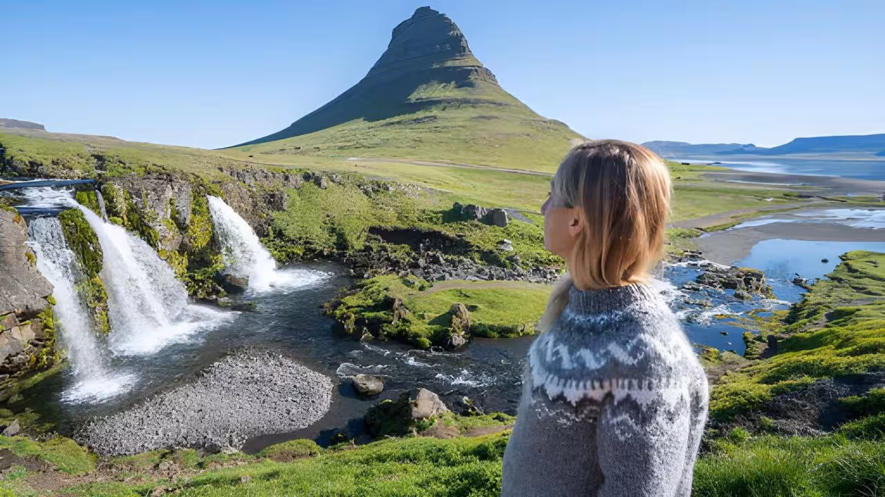 Woman in Icelandic sweater admiring Kirkjufellsfoss waterfall and Kirkjufell mountain on Snaefellsnes peninsula