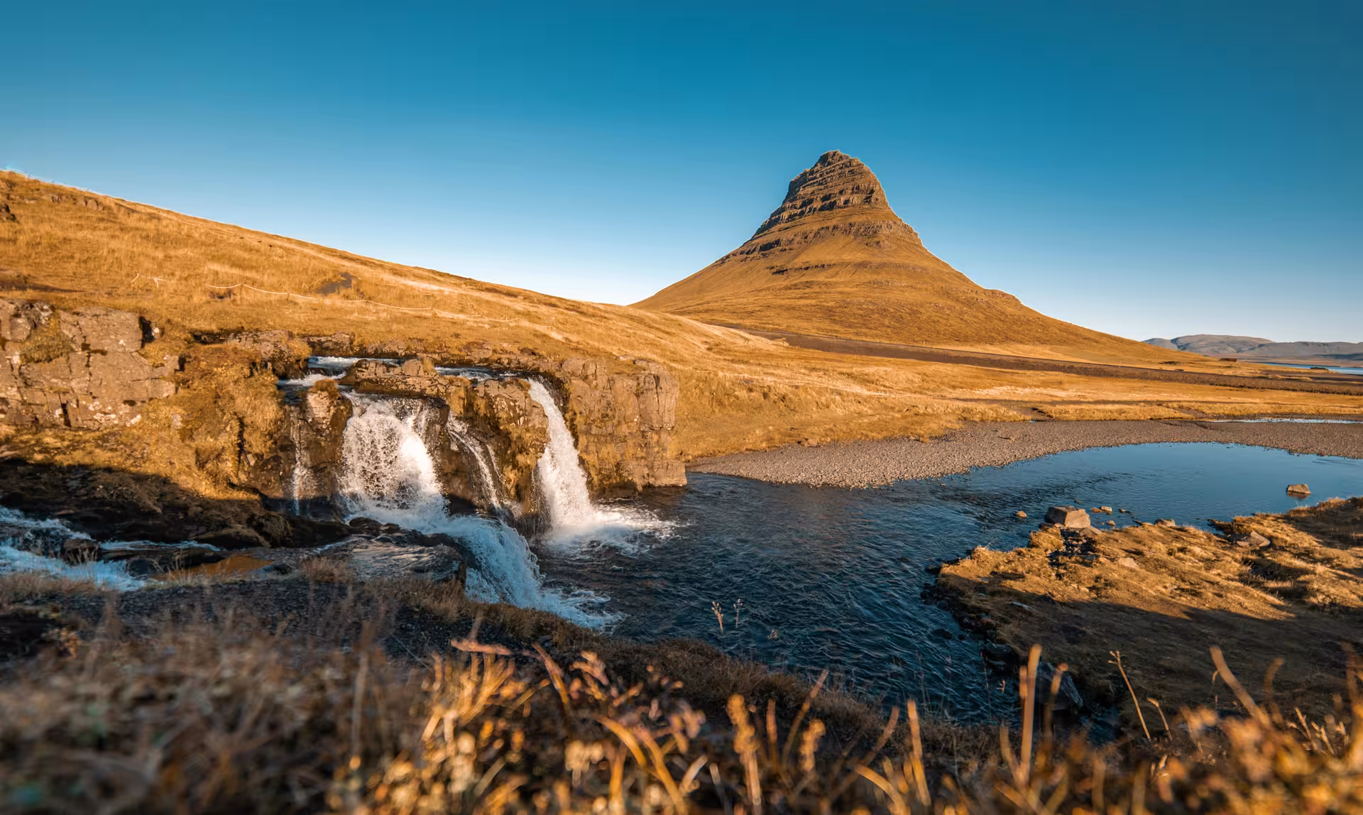 Kirkjufellsfoss waterfall cascading beside Kirkjufell mountain on Iceland's Snaefellsnes Peninsula under clear blue sky