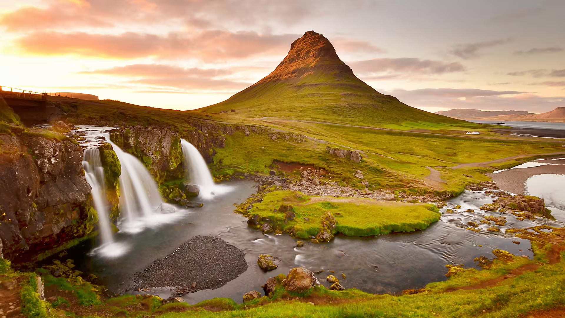 Kirkjufell mountain with cascading waterfalls and green landscape at sunset in Snaefellsnes Iceland