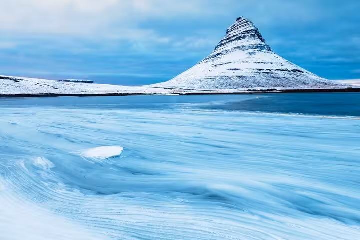 Snow-covered Kirkjufell mountain rising above a frozen blue lagoon on Snaefellsnes Peninsula, Iceland