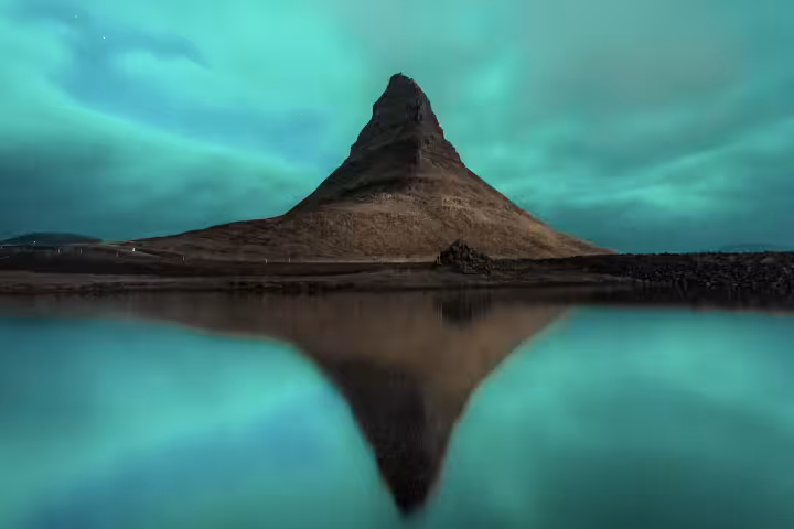 Northern lights glowing over iconic Kirkjufell mountain reflected in calm waters on a Snaefellsnes Peninsula Iceland tour
