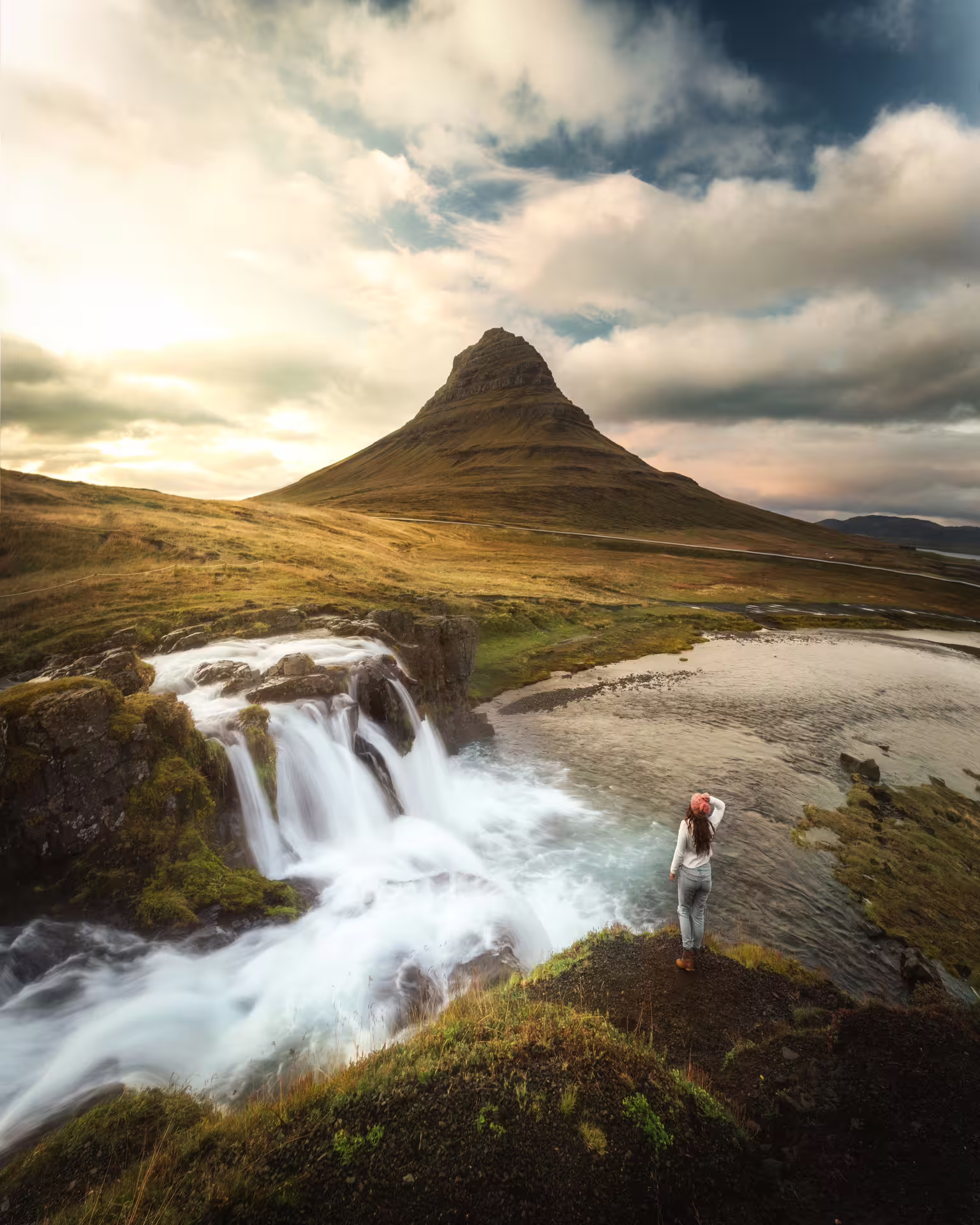 Traveler admiring Kirkjufellsfoss waterfall with iconic Kirkjufell mountain on Snaefellsnes Peninsula Iceland tour