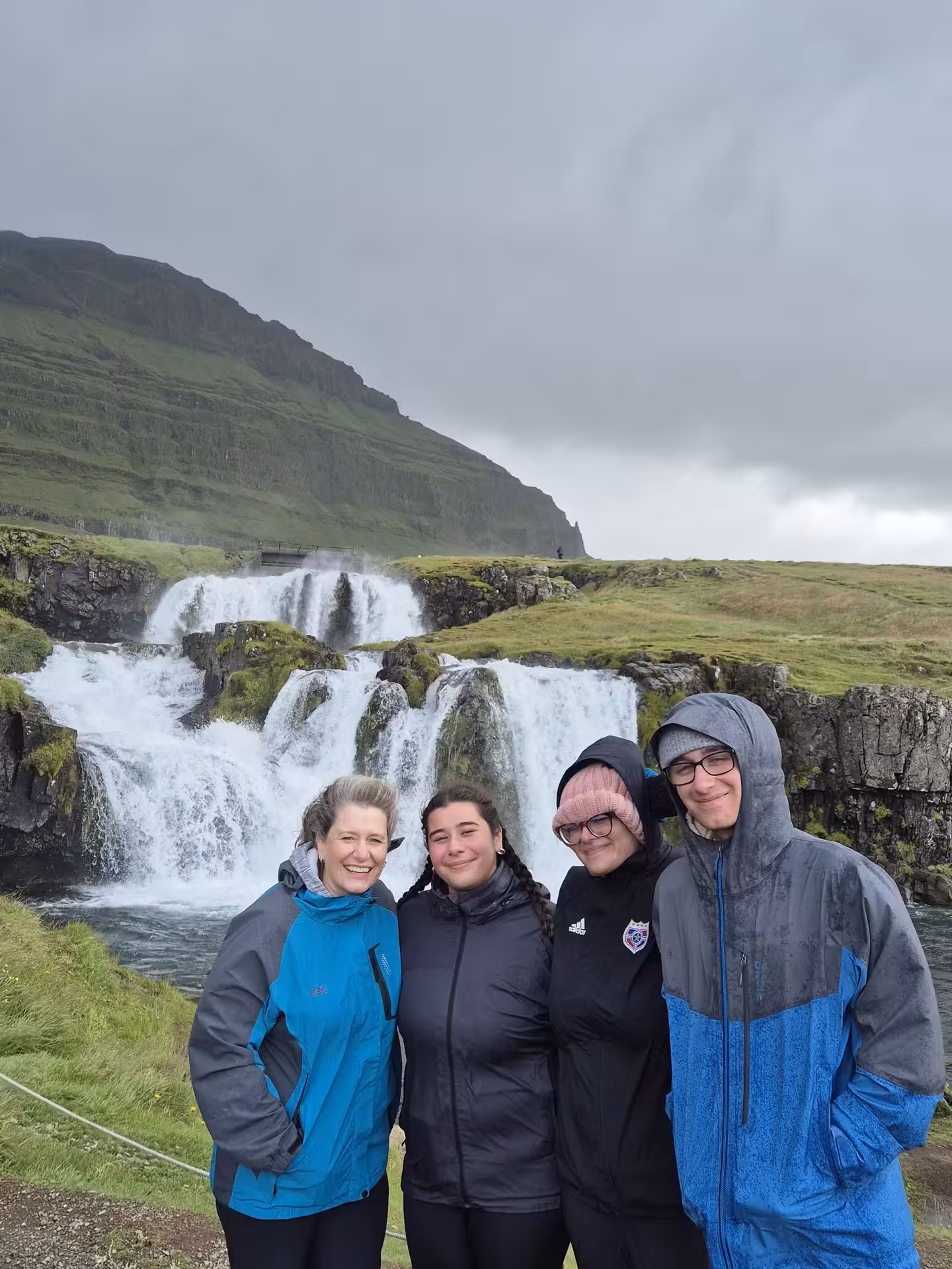 Four tourists smiling in front of Kirkjufellsfoss waterfall on Snaefellsnes Peninsula, Iceland