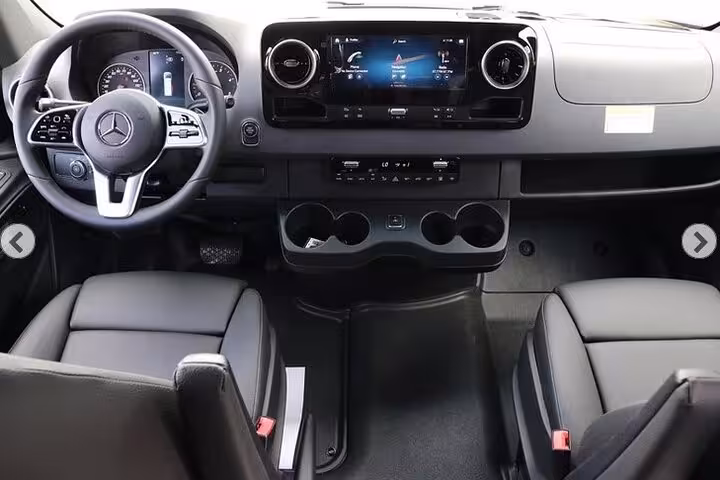 Modern dashboard and front seating of a private KOA airport transfer van featuring advanced controls for a luxury ride.