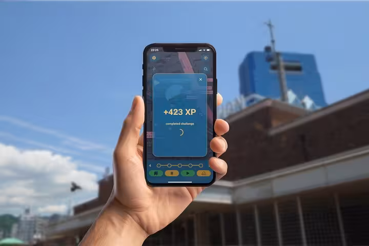 Hand holding smartphone showing +423 XP completed challenge screen from a self-guided walking tour mobile game in Kobe
