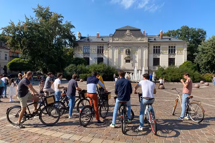 Cyclists gather in front of historic building in Krakow during guided bike tour, enjoying cultural landmarks and sunny weather.