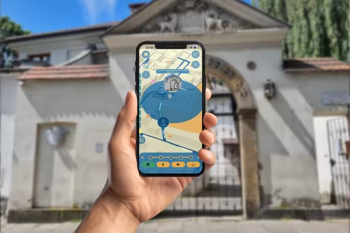Hand holding smartphone with interactive map app in front of historic Kazimierz Jewish Quarter gate in Krakow