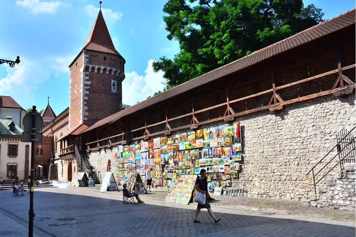 Art paintings displayed along medieval city walls near a brick tower in Krakow Old Town