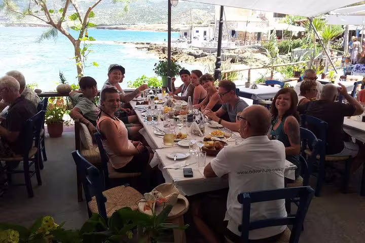 Tour group dining at a seaside restaurant in Kritza, savoring local cuisine with stunning coastal views.