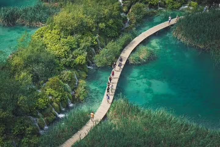 Group walking the wooden boardwalk over turquoise lakes at Plitvice Lakes, guided group adventure from Split