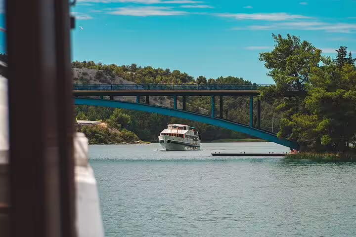 Boat cruise on the Krka River under a bridge, part of the scheduled Krka Waterfalls food and wine tour