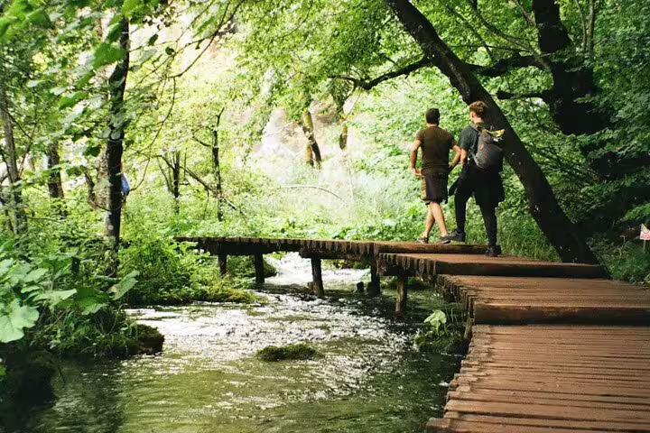 Hikers on wooden boardwalk over stream in Plitvice Lakes, guided group day trip from Split, Croatia