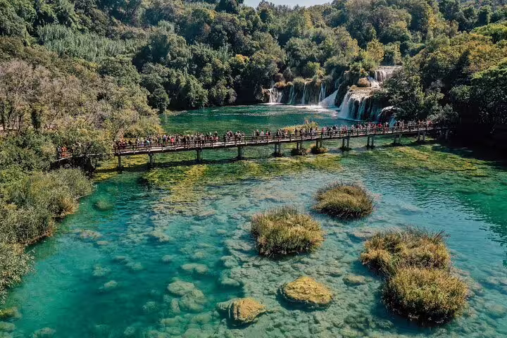 Wooden boardwalk over turquoise Krka National Park pools with waterfalls, on scheduled boat cruise and swim tour