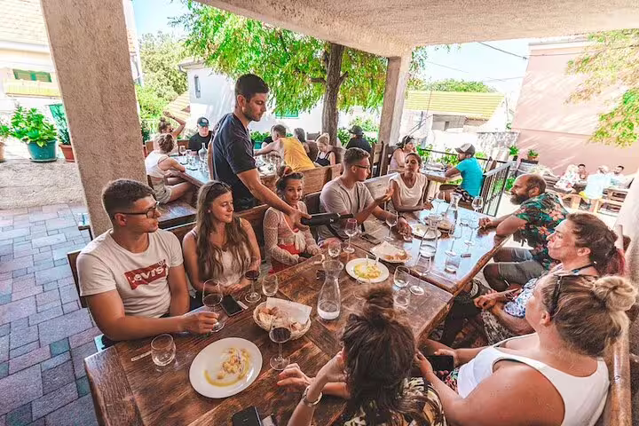 Travelers share local dishes and Croatian wine tasting on Krka Waterfalls day trip, seated on a shaded terrace