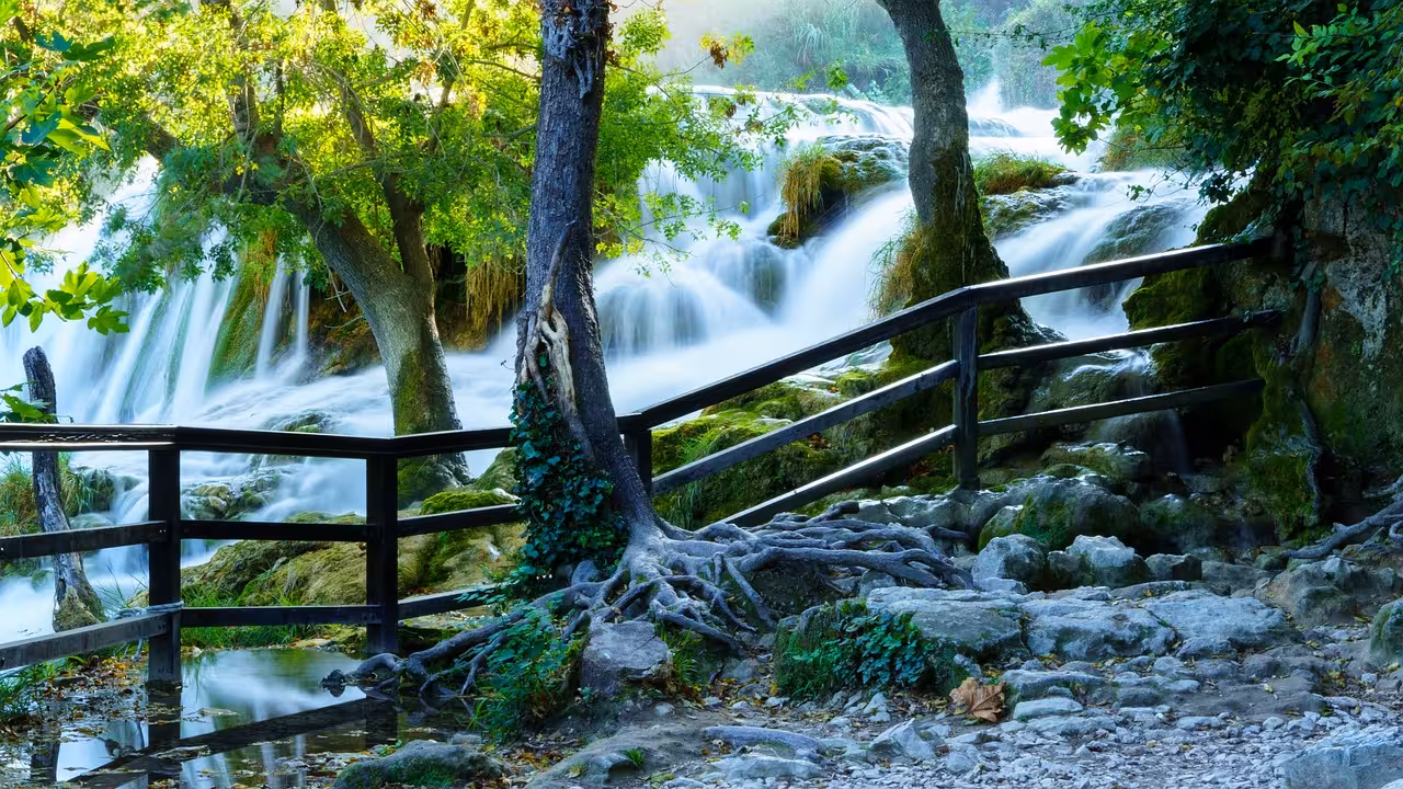Wooden footbridge beside rushing Krka Waterfalls in Krka National Park, highlight of the Skradin day trip
