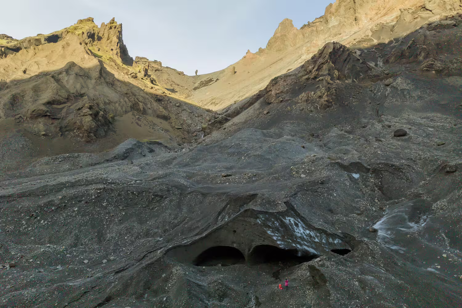 Vast ash-covered glacier surface with ice caves and tiny explorer at Krossarjokull citizen science tour Iceland