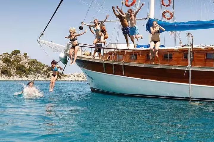Group of tourists joyfully jumping off a boat into the crystal-clear waters on a Kusadasi boat trip.
