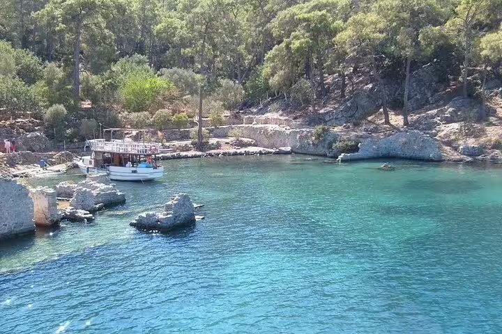 Idyllic bay view from Kusadasi boat tour with a docked boat and lush green forest backdrop.