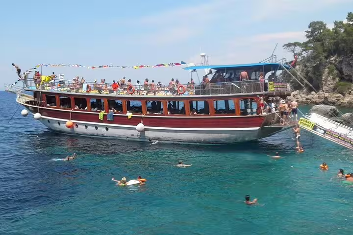 Tourists swimming and relaxing around a traditional boat on a sunny Kusadasi National Park excursion.