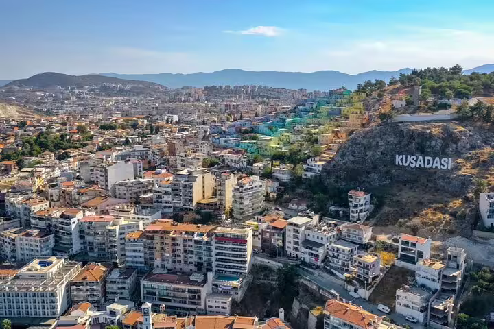 Aerial view of Kusadasi city with colorful hillside buildings and large Kusadasi sign on rocky hill, Turkey