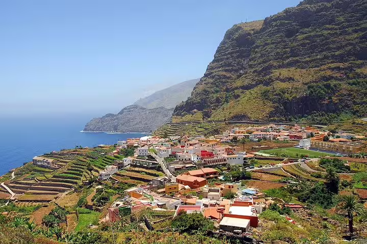 Charming village nestled in terraced hills overlooking the ocean on La Gomera, under a bright blue sky.