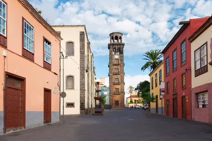 Charming street in La Laguna, Tenerife, featuring colorful buildings and a historic clock tower under a blue sky.