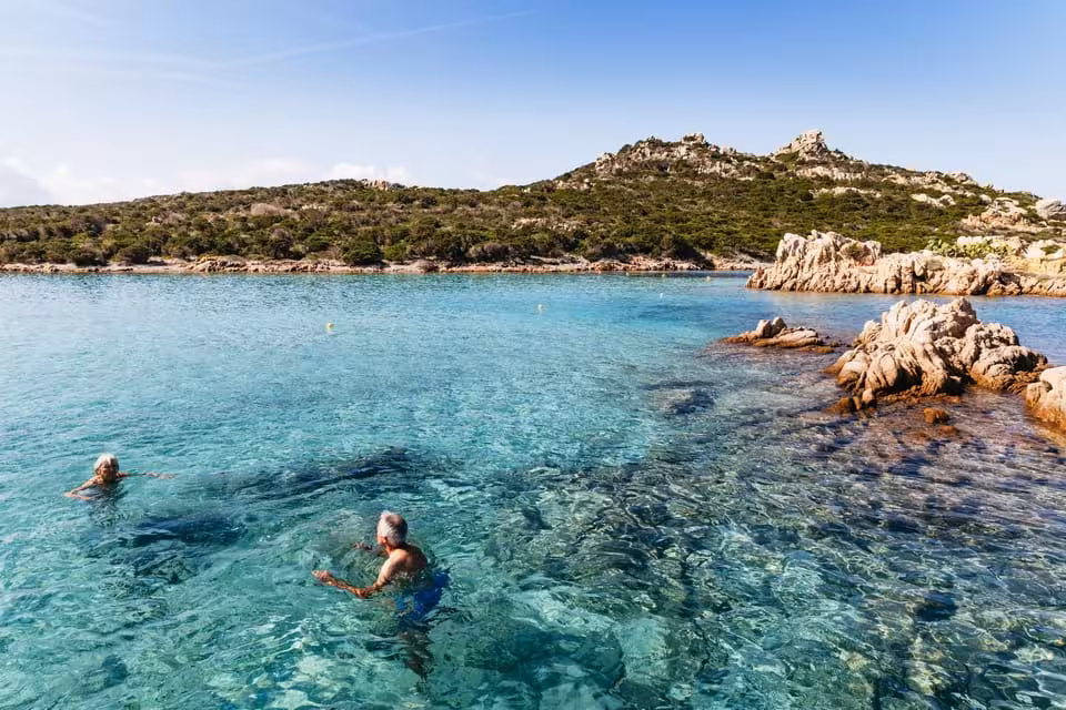 Tourists swimming in crystal-clear waters with rocky islands in the background at La Maddalena Archipelago.